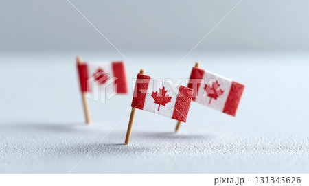 Three miniature canadian flags are standing on toothpicks on a textured white surface, creating a patriotic display representing canada's national identity and celebrating its cultural heritage 131345626