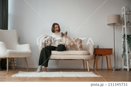 Front view, sitting on the little sofa. Young woman is with her pug dog at home 131345731
