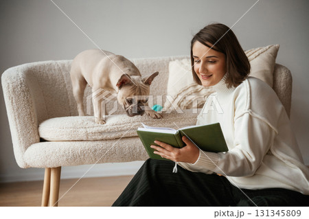 Reading the book. Young woman is with her pug dog at home 131345809