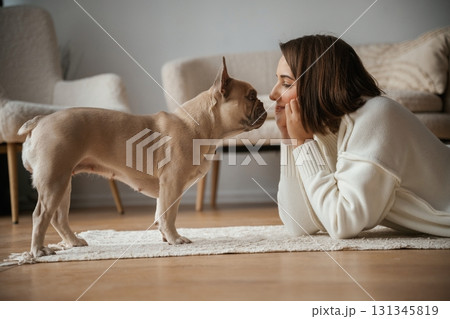 Looking at each other, lying down on floor. Young woman is with her pug dog at home 131345819