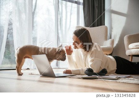 With laptop. On the floor. Young woman is with her pug dog at home 131345828