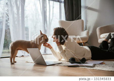 With laptop. On the floor. Young woman is with her pug dog at home With laptop. On the floor. Young woman is with her pug dog at home 131345833