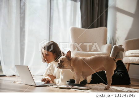 Wooden floor. With laptop. Young woman is with her pug dog at home 131345848