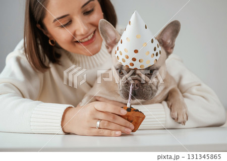 Happy birthday. Pet in hat and with cake. Young woman is with her pug dog at home 131345865