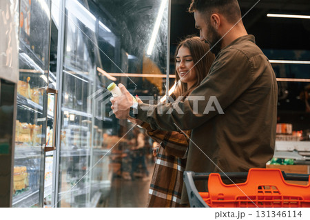 Side view, choosing products. Young couple are in supermarket together Side view, choosing products. Young couple are in supermarket together 131346114