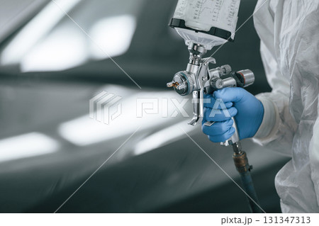Focused close up view. Man is holding spray gun for painting a car 131347313