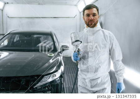 Bright artificial lighting. Man is standing and holding spray gun with paint for automobile 131347335