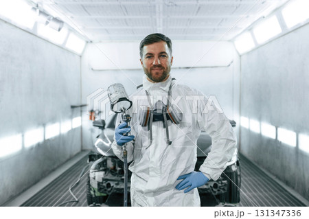 Bright artificial lighting. Man is standing and holding spray gun with paint for automobile Bright artificial lighting. Man is standing and holding spray gun with paint for automobile 131347336
