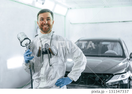 Bright artificial lighting. Man is standing and holding spray gun with paint for automobile Bright artificial lighting. Man is standing and holding spray gun with paint for automobile 131347337