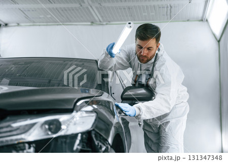 Front view. Garage worker is holding lighting and checking surface of the car Front view. Garage worker is holding lighting and checking surface of the car 131347348