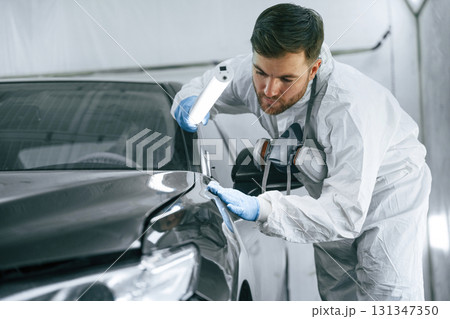 Front part of the automobile. Garage worker is holding lighting and checking surface of the car 131347350