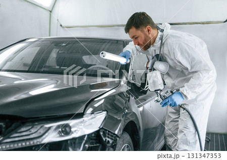 By help of lighting equipment. Man is painting a car by using spray guy By help of lighting equipment. Man is painting a car by using spray guy 131347353