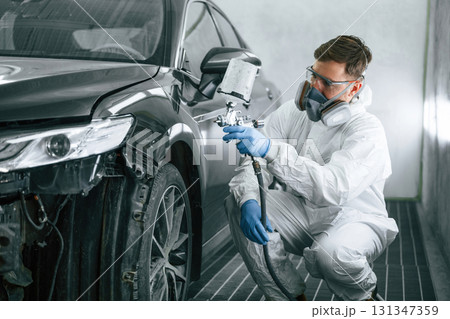 Professional worker. Man is painting a car by using spray guy Professional worker. Man is painting a car by using spray guy 131347359