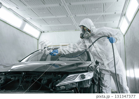 White protective wear. Man is painting a car by using spray guy 131347377