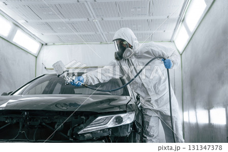 White protective wear. Man is painting a car by using spray guy 131347378
