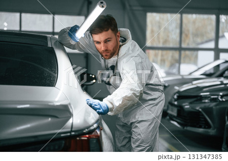 Rear part of automobile. Garage worker is holding lighting and checking surface of the car Rear part of automobile. Garage worker is holding lighting and checking surface of the car 131347385