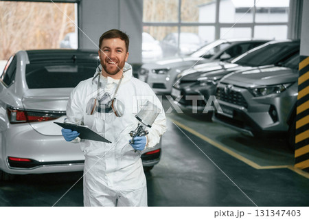 Portrait of car painter that is standing in the garage with documents in hands Portrait of car painter that is standing in the garage with documents in hands 131347403