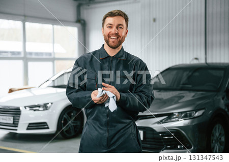 Handsome friendly guy. Repairman in uniform is standing in the garage with cars 131347543