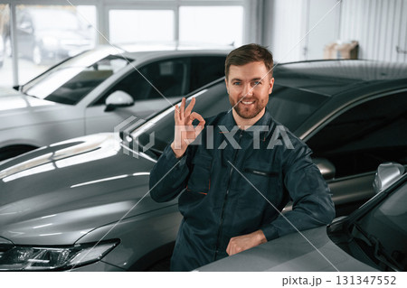 Repairman in uniform is standing in the garage with cars Repairman in uniform is standing in the garage with cars 131347552