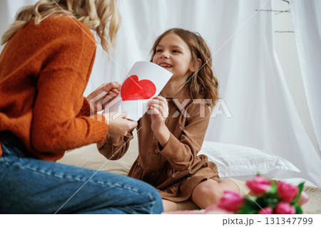 Red paper heart shaped present for mother's day. Female parent with daughter is at home Red paper heart shaped present for mother's day. Female parent with daughter is at home 131347799
