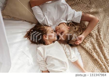 Top view, lying down on the bed. Mother with daughter are at home together Top view, lying down on the bed. Mother with daughter are at home together 131347964
