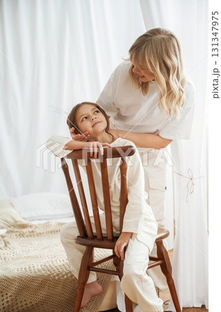 On the wooden chair. Mother with daughter are at home together 131347975