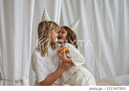 In festive hats, celebrating birthday. Mother with daughter are at home together 131347993
