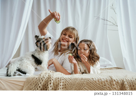 Playing with little dog. Cucumbers beauty procedure conception. Mother with daughter are at home Playing with little dog. Cucumbers beauty procedure conception. Mother with daughter are at home 131348015