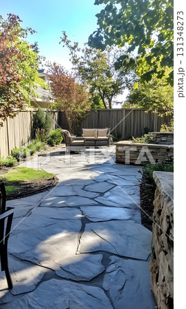 Stone patio leads to backyard furniture set surrounded by lush green trees in summer Stone patio leads to backyard furniture set surrounded by lush green trees in summer 131348273