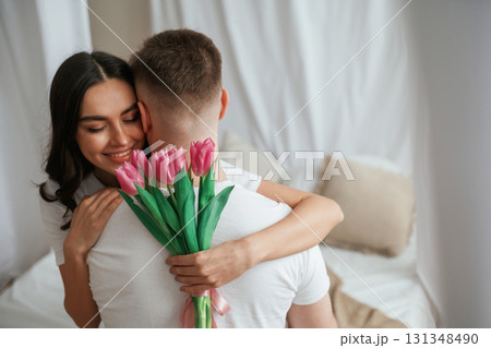 Pink flowers in hands. Young couple are together at home Pink flowers in hands. Young couple are together at home 131348490