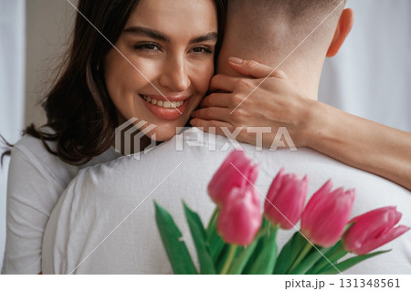 Woman is holding flowers and embracing the man. Young couple are together at home 131348561