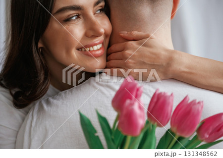 Woman is holding flowers and embracing the man. Young couple are together at home Woman is holding flowers and embracing the man. Young couple are together at home 131348562