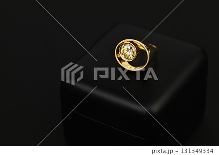 A gold ring with a yellow diamond in the center sits on a black background 131349334