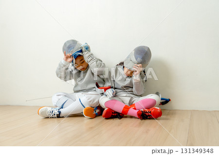Asian boy and girl with fencing sport uniform sit beside on the floor and take mask off to relax after practice for competition. 131349348