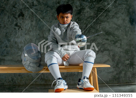 Asian boy with fencing sport uniform hold epee and point to his front side during relax from practice. 131349355