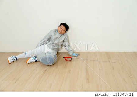 Asian boy with fencing sport uniform sit on the floor and look tired also relax after practice for competition. Asian boy with fencing sport uniform sit on the floor and look tired also relax after practice for competition. 131349421