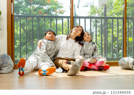 Asian mother, boy and girl as family sit on the floor in front of glass door and look up with happiness after relax of practice in their house. 131349459