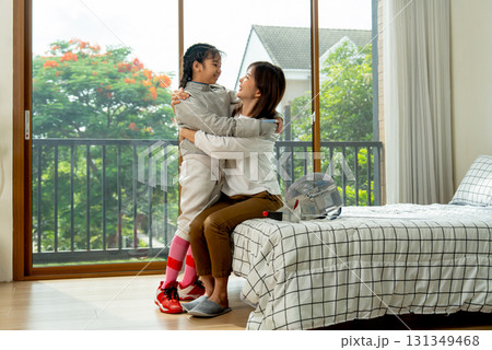 Asian mother sit on bed and hug together with her daughter during practice fencing sport in bedroom with soft morning light and happiness. Asian mother sit on bed and hug together with her daughter during practice fencing sport in bedroom with soft morning light and happiness. 131349468