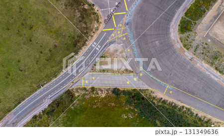 Aerial view of curved and straight roads with traffic markings, arrows, and signs, set in grassy terrain possibly a test track or training site. Aerial view of curved and straight roads with traffic markings, arrows, and signs, set in grassy terrain possibly a test track or training site. 131349636