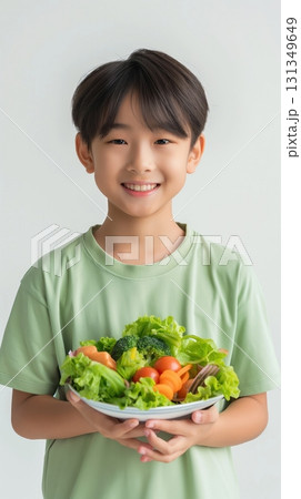 A young boy is holding a bowl of vegetables, including broccoli and carrots 131349649