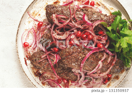 grilled kebabs topped with onions and pomegranate on a white plate in a bright kitchen setting 131350937