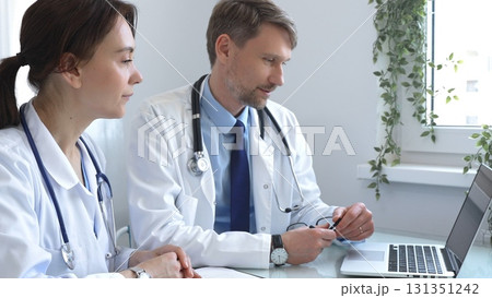 Two doctors are carefully studying medical charts on a laptop, discussing patient medical histories in a hospital or clinic. Medicine and healthcare concept. Two doctors are carefully studying medical charts on a laptop, discussing patient medical histories in a hospital or clinic. Medicine and healthcare concept. 131351242