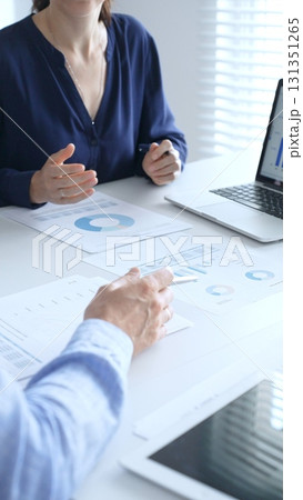 Businessman and businesswoman are analyzing financial data on a laptop and looking through documents, pointing at charts and graphs during a meeting in bright office. Business people concept Businessman and businesswoman are analyzing financial data on a laptop and looking through documents, pointing at charts and graphs during a meeting in bright office. Business people concept 131351265