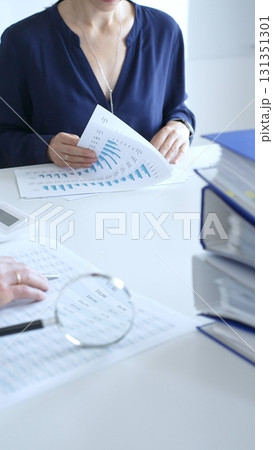 Two professional accountants analyzing financial reports with magnifying glass and calculator, performing accounting and auditing tasks in the office, close up of hands. Audit and taxes in business Two professional accountants analyzing financial reports with magnifying glass and calculator, performing accounting and auditing tasks in the office, close up of hands. Audit and taxes in business 131351301