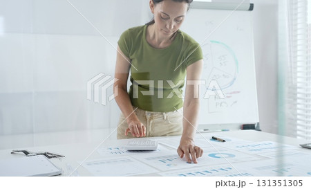 Businesswoman pointing at financial charts and graphs on a table, with a pie chart on a flip chart in the background. Business people concept Businesswoman pointing at financial charts and graphs on a table, with a pie chart on a flip chart in the background. Business people concept 131351305