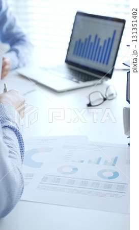 Two professional auditors reviewing financial documents, working collaboratively at white desk with blue folder stack, highlighting teamwork. Audit and taxes in business 131351402