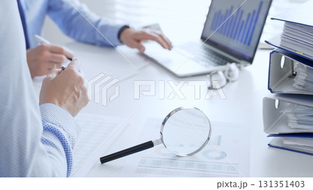 Business team working together, analyzing financial data on charts and documents, laptop and folders on white desk in office, close up of magnifying glass. Audit and taxes theme in business 131351403
