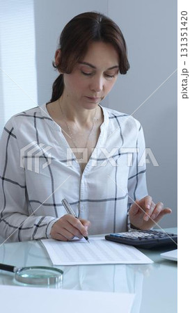 Female professional calculating finances, reviewing paperwork, tracking business expenses with precision and focus. Audit and taxes in business 131351420