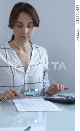Accountant carefully reviewing financial documents, magnifying details, calculating performance metrics at professional workspace. Audit and taxes in business Accountant carefully reviewing financial documents, magnifying details, calculating performance metrics at professional workspace. Audit and taxes in business 131351427