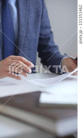 Closeup of businessman hands signing a contract with elegant pen, wearing a blue suit and a wristwatch, sitting at a white desk in office. Business people concept 131351462